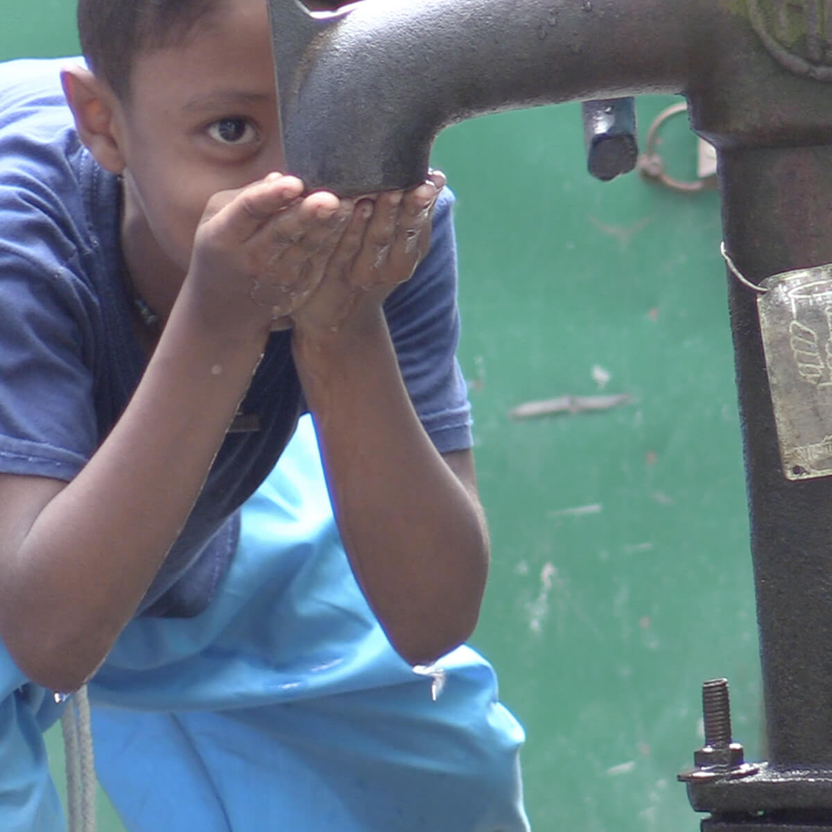 Boy cupping his hands to drink from water pump.